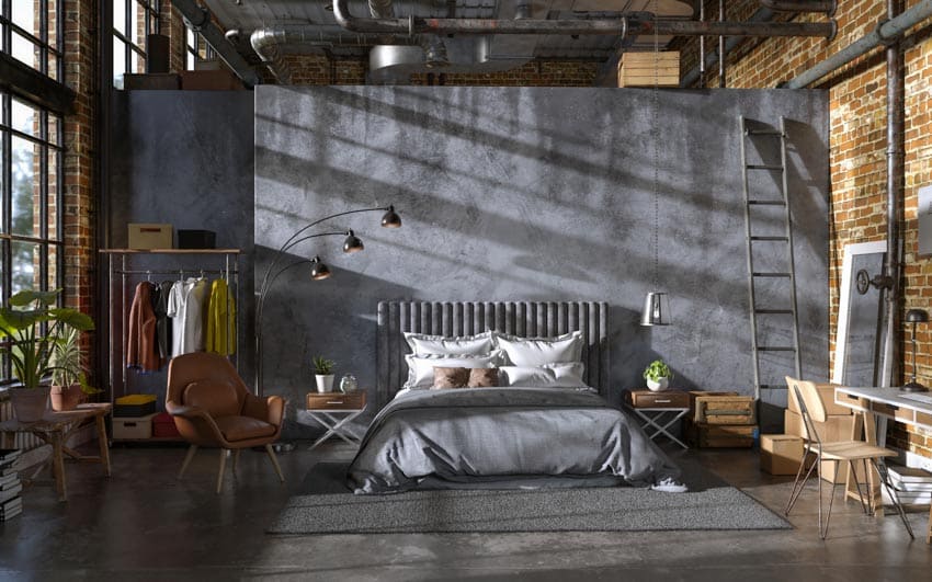 Industrial bedroom with bed, comforter, headboard, pillows, brick wall, chair, concrete wall, floors, window, and lamp