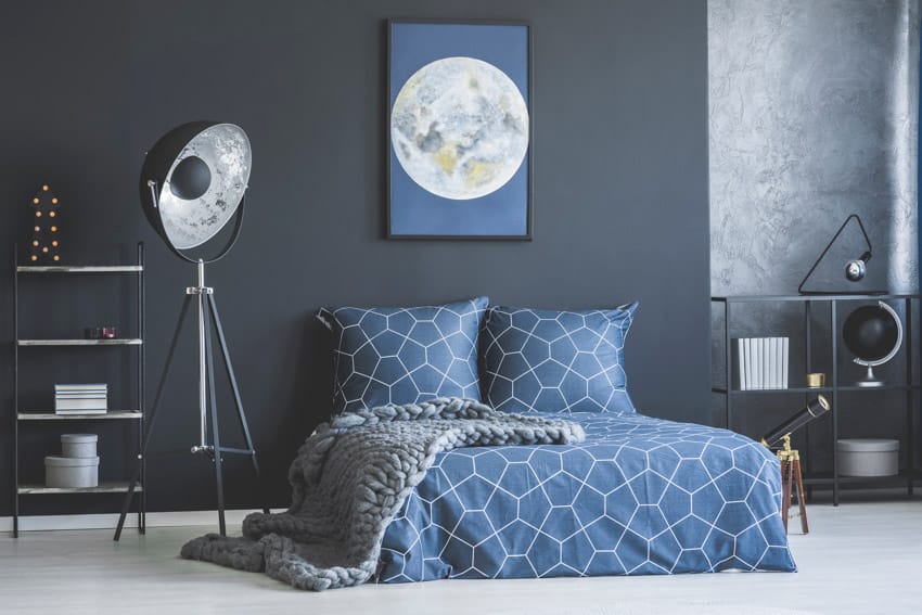 Industrial bedroom with blue paint wall color, bedding, pillows, floor lamp, and freestanding shelves