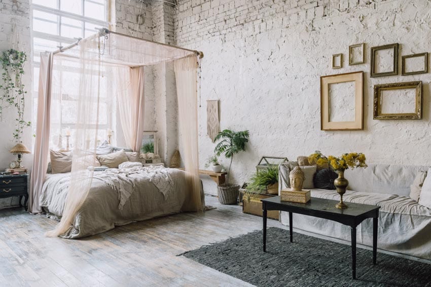 Industrial bedroom with feminine decor, bed, couch, coffee table, rug, indoor plants, brick wall, and window