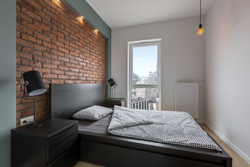 Industrial bedroom with masculine decor, brick wall, headboard, pillows, bedding, nightstand, lamp, and window