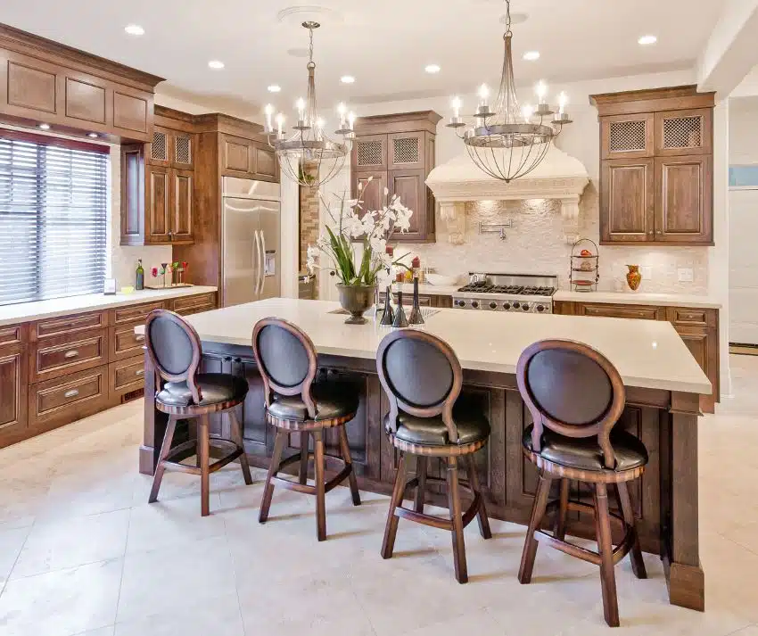 Interior design of a luxury traditional kitchen features chandeliers with candlestick holders on top of island counter and chairs