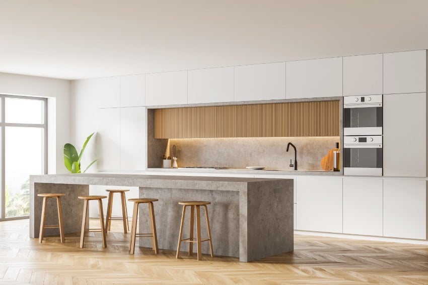 Modern kitchen with white walls, glass windows, wooden parquet floor, bar counter, and two ovens