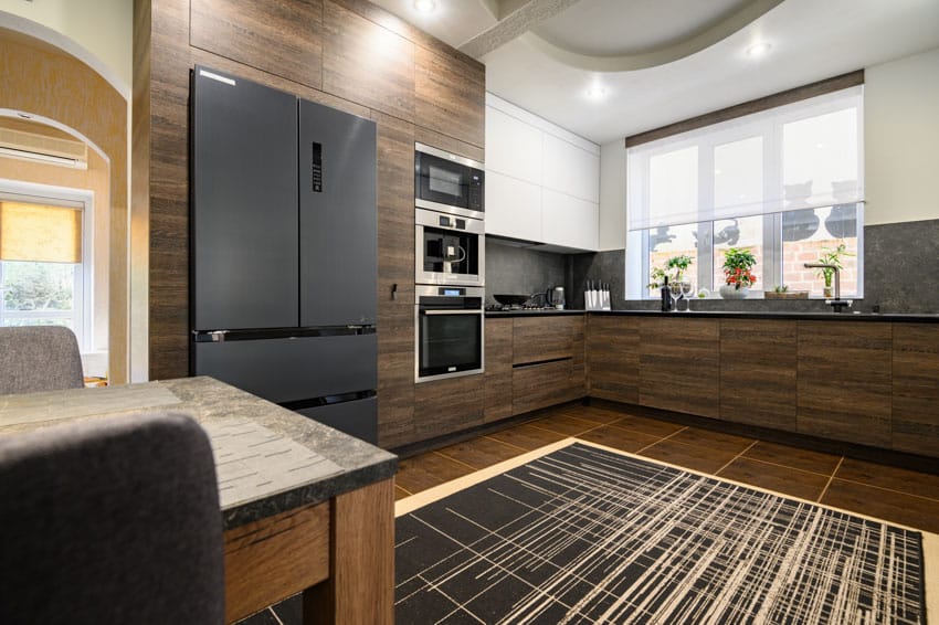 Kitchen with laminate cabinets, black refrigerator, rug, countertop, backsplash, and window
