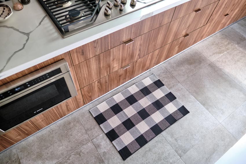 Kitchen with patterned mat, concrete tile floor, wood cabinets, countertop, and oven