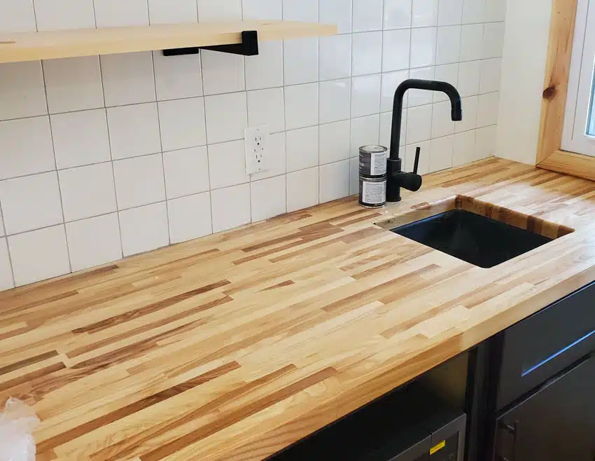 Kitchen with square tile backsplash, cedar countertop, sink, faucet, and cabinets