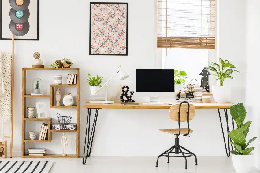 Large industrial desk with a computer by a window a wooden alder bookcase and posters on a white wall in a stylish, scandi home office interior