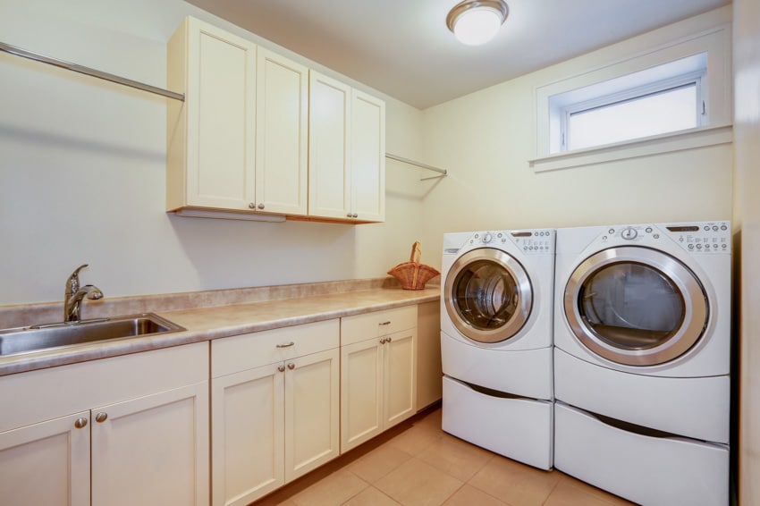 Laundry room with washing machines, countertop, cabinets, sink, faucet, ceiling light, and hopper window