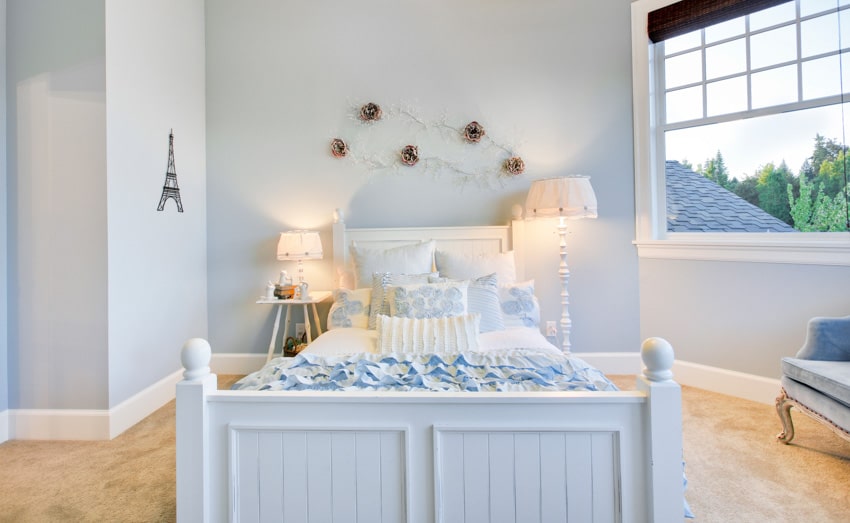 Light blue bedroom with nightstand, footboard, lamps, wooden flooring, and window