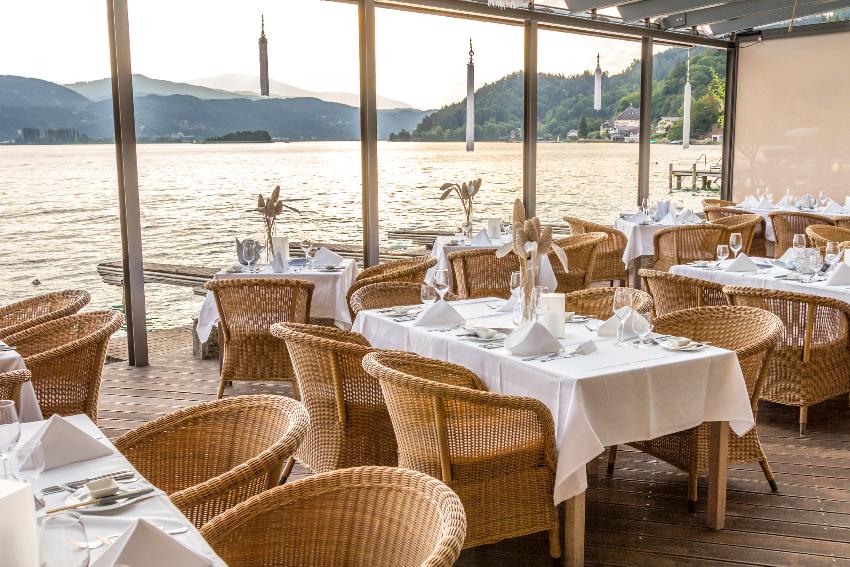 Luxurious restaurant features beautiful table set up with white cotton tablecloth and rattan chairs on pier at a lake