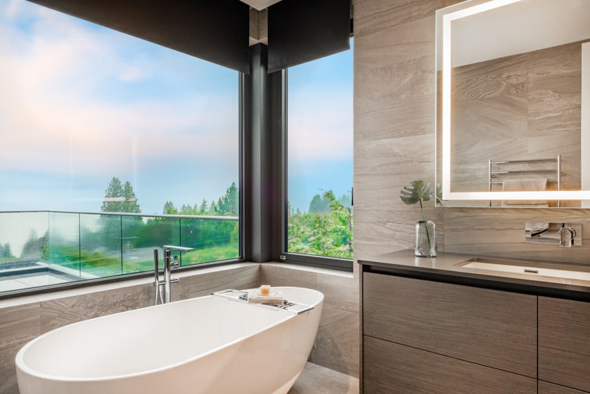 Luxury bathroom with tub, mirror, countertop, cabinet, window, and wide spread bathtub faucet