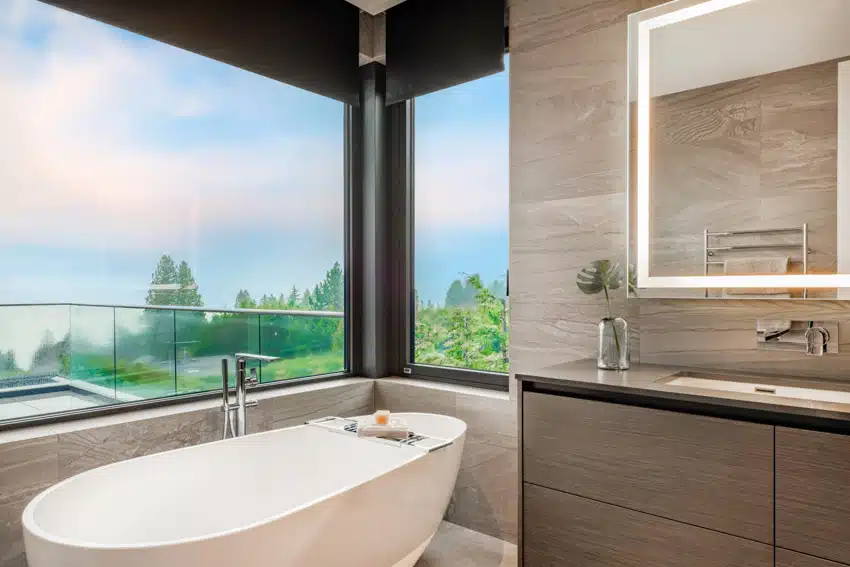 Luxury bathroom with tub, mirror, countertop, cabinet, window, and wide spread bathtub faucet