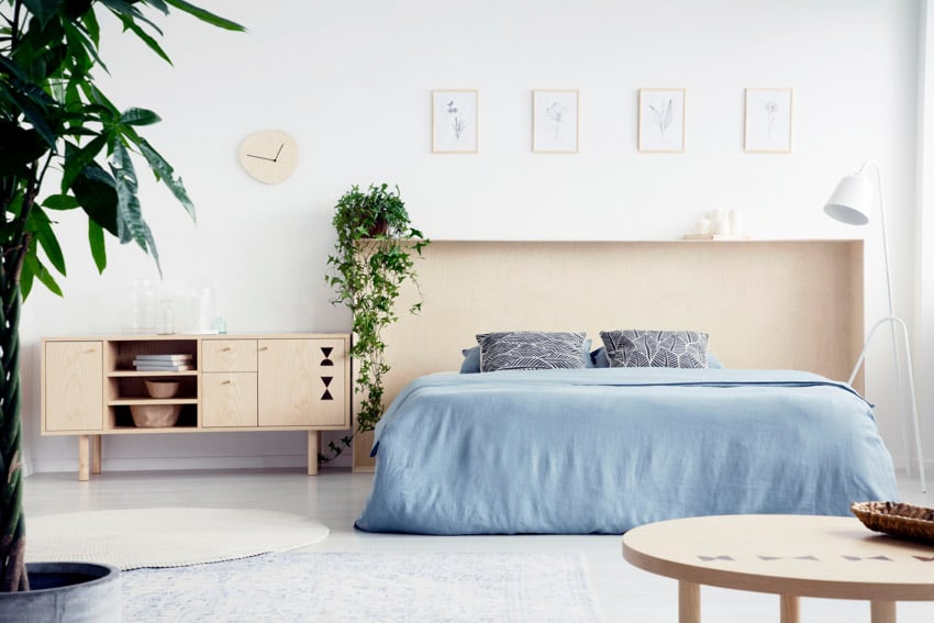 Minimalist bedroom with plywood headboard, console table, mattress, pillows, and indoor plants