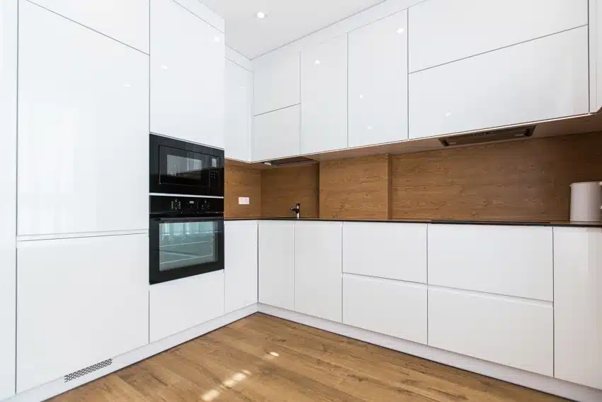 Minimalist kitchen with wood floors, oven, white cabinets, and wooden laminate backsplash
