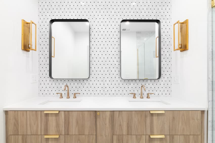 Bathroom with wall scones in gold, twin mirrors and cabinets with gold handles