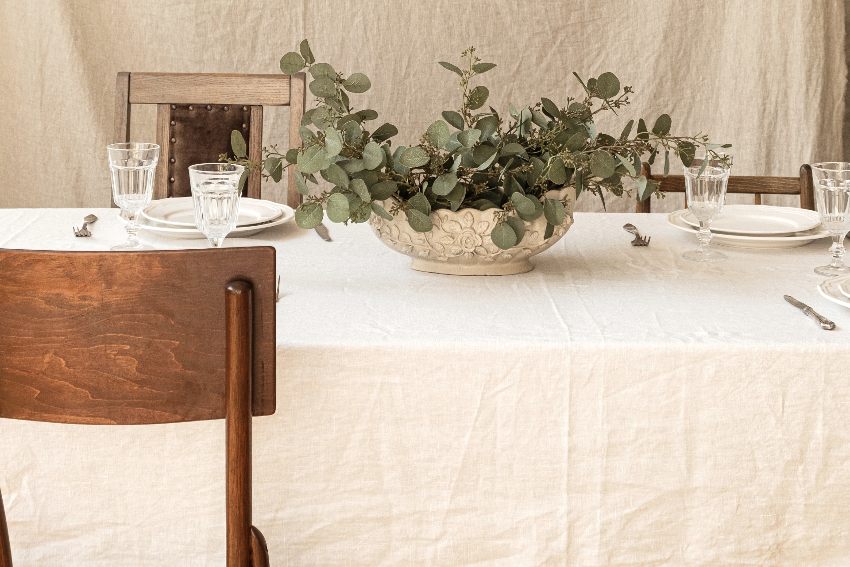 Modern interior dining room design with bohemian styled decorations dinner table, eucalyptus branches, wineglasses, plates cutlery on linen tablecloth