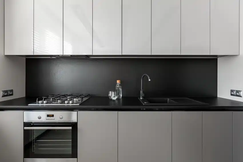 Modern kitchen with black laminate backsplash, countertop, oven, stove, cabinets, sink, and faucet