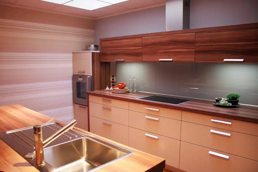 Modern kitchen with cedar countertop, cabinets, glossy backsplash, sink, faucet, stove, and range hood