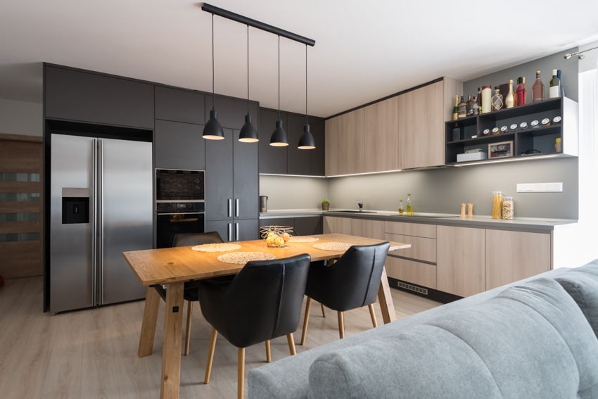 Modern kitchen with dining space, maple wood table, black chairs, refrigerator, backsplash, countertop, and pendant lights