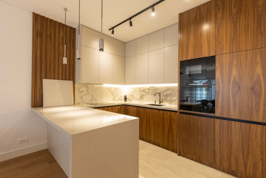 Modern kitchen with laminate cabinets, track lighting, oven, marble backsplash, countertop, sink, and faucet