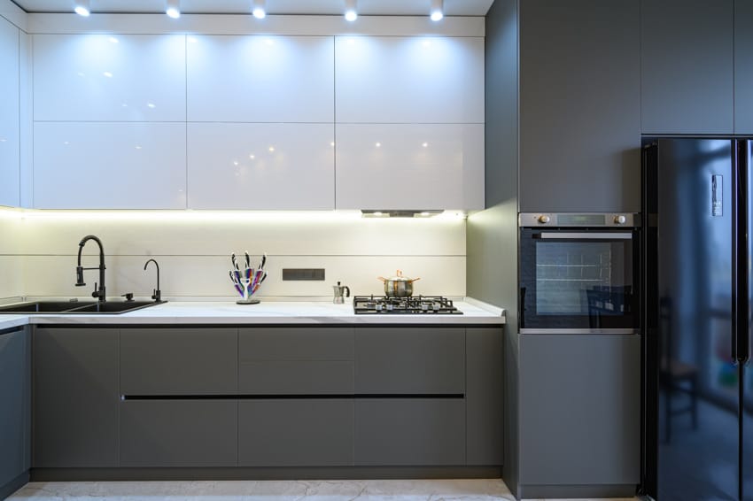 Modern kitchen with mismatched cabinets, backsplash, countertop, sink, faucet, refrigerator, and under cabinet lighting