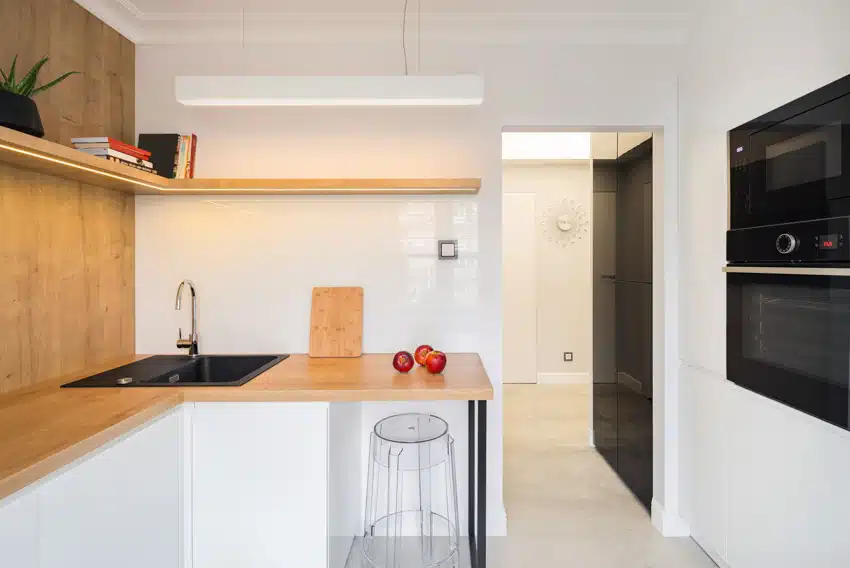 Modern kitchen with rubberwood butcher block countertop, floating shelves, wood backsplash, oven, cutting board, and bar stool