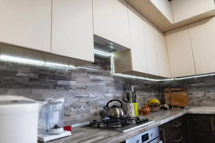 Modern kitchen with stacked stone veneer backsplash, white cabinets, countertop, and stove