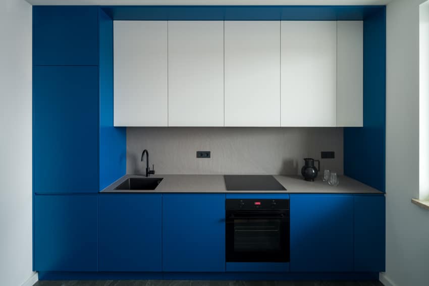 Modern kitchen with white and blue cabinets, countertop, oven, induction stove, sink, faucet, and laminate backsplash