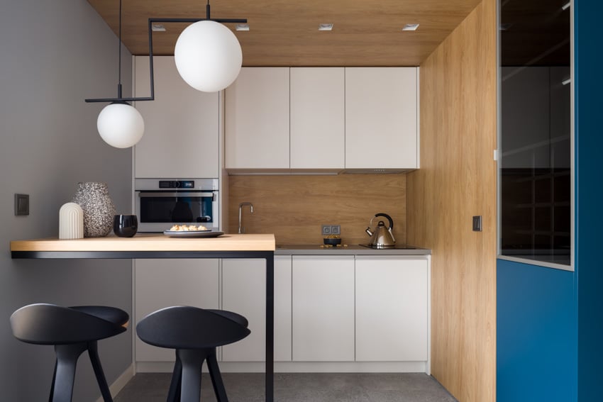Modern kitchen with white cabinets, bar counter, stools, pendant lights, and laminate backsplash