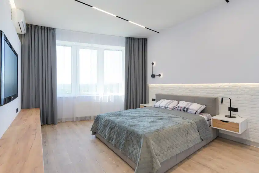 Modern light blue bedroom with wood flooring, ceiling lights, floating nightstand, and wall sconce
