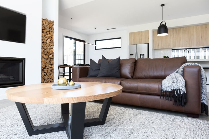 Modern living room with brown leather sofa, birch wood coffee table, fireplace, and pendant lights