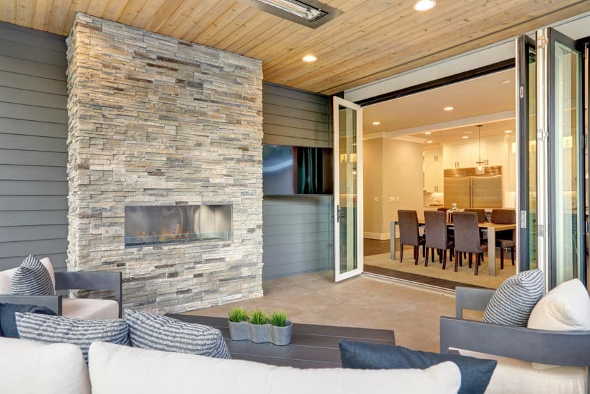 Outdoor patio with ledger stone fireplace, siding, wood beadboard ceiling, folding glass patio doors, and sofa