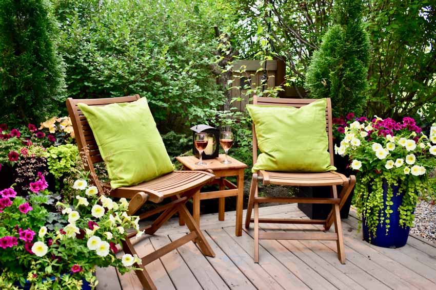 Outdoor patio with mahogany folding chairs, flowers, and hedge plants