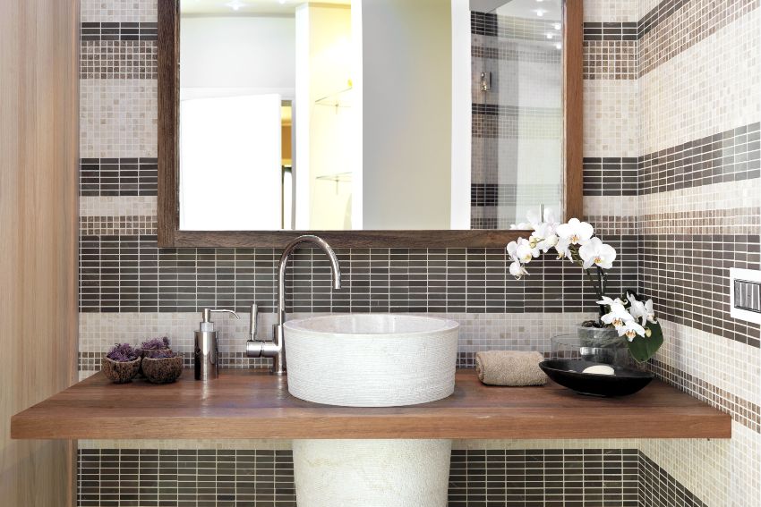 Pedestal sink with backsplash in modern bathroom with a vase of white orchid