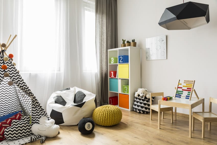 Playroom with kids bean bag chair, wood chairs, freestanding shelves, small tent, pendant light, window curtains, and wooden flooring