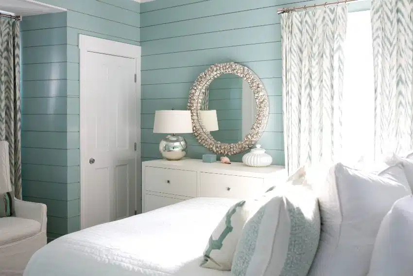 Bedroom with white and teal tones, roound mirror and curtains