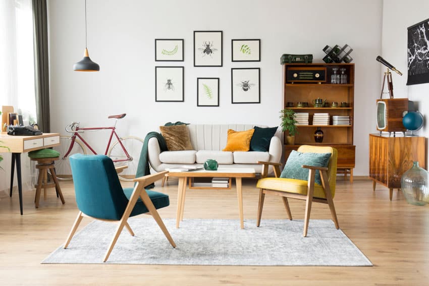 Retro inspired living room with softwood furniture, rug, cushioned chairs, sofa, desk, pendant light, bookshelf, and wood floors