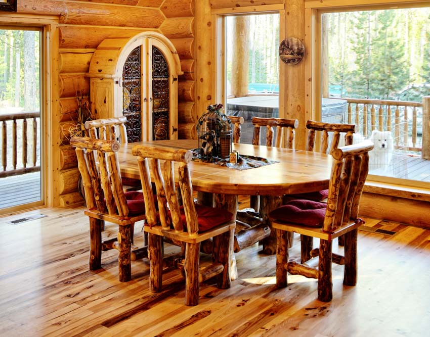 Rustic dining room with aspen wood table, chairs, log wall, glass cabinets, windows, and wooden flooring