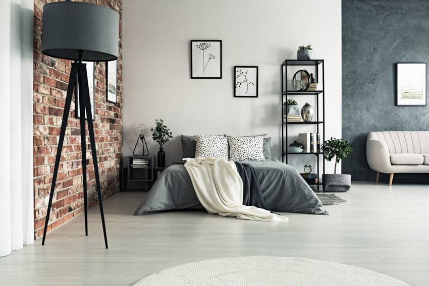 Rustic industrial bedroom with floor lamp, brick wall, bed, pillows, nightstand, and freestanding shelf