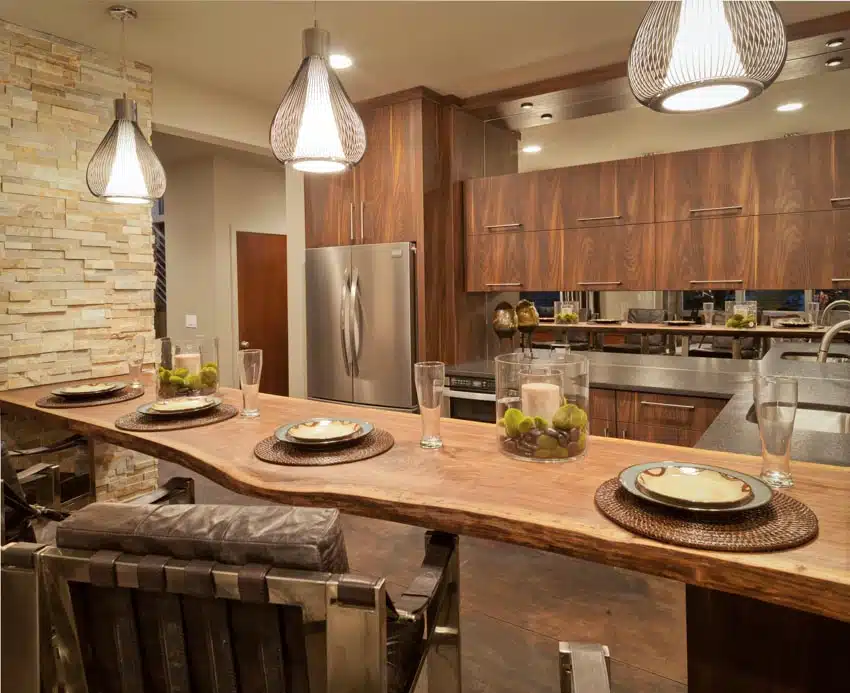 Rustic kitchen with cedar live edge countertop, chairs, plates, wood cabinets, refrigerator, accent wall, and pendant lights