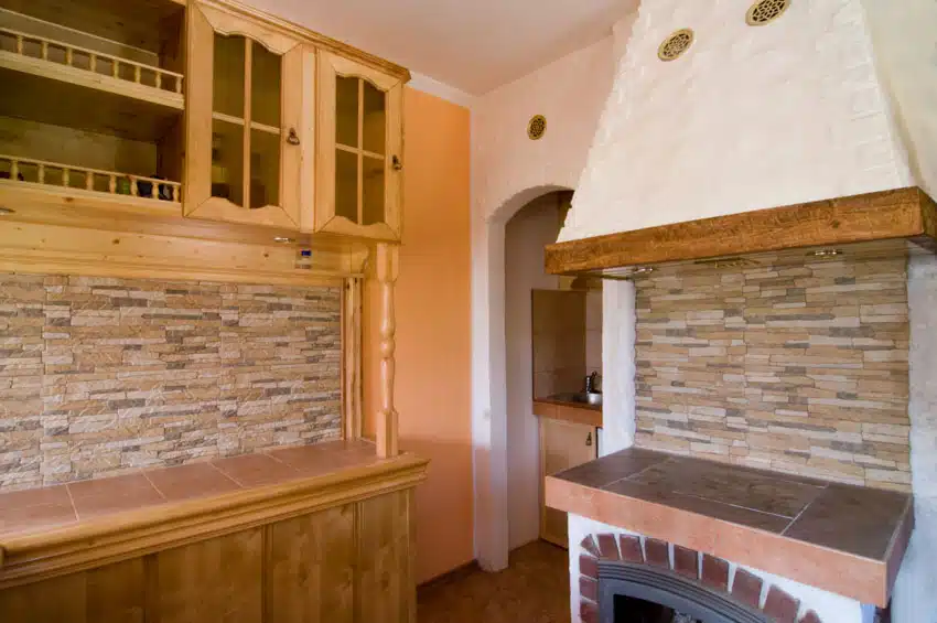 Rustic kitchen with dry stacked stone backsplash, cabinets, range hood, and countertop