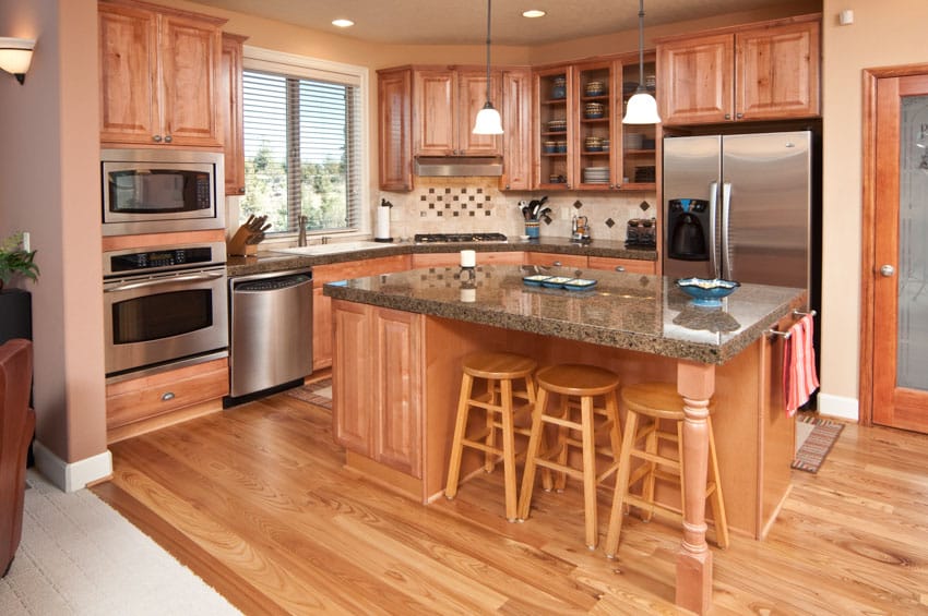 Rustic kitchen with octagon backsplash, island, bar stools, wood floor, cabinets, oven, dishwasher, pendant lights, refrigerator, and window