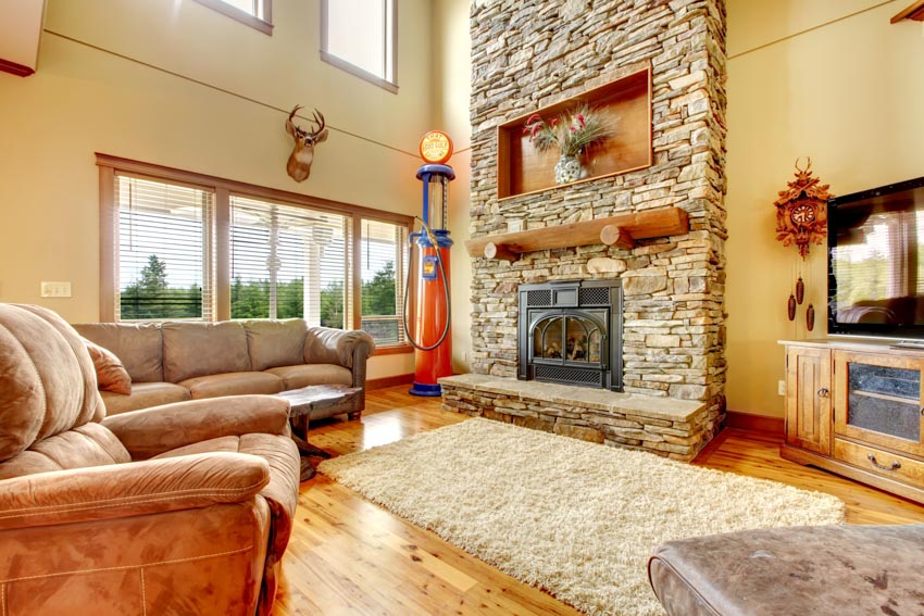 Rustic living room with ledger stone fireplace, rug, sofa, lamp, wood flooring, and windows