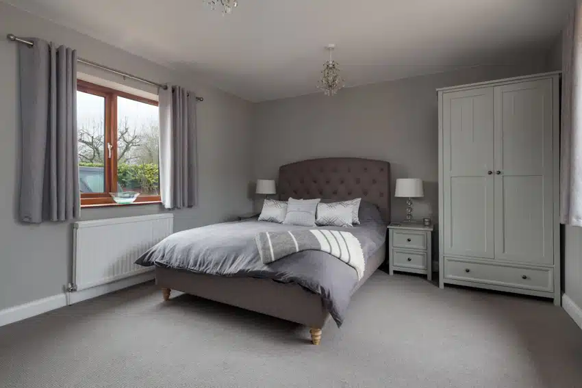 Bedroom with nightstand, grey comforter, tufted headboard, white lamps and sliding window