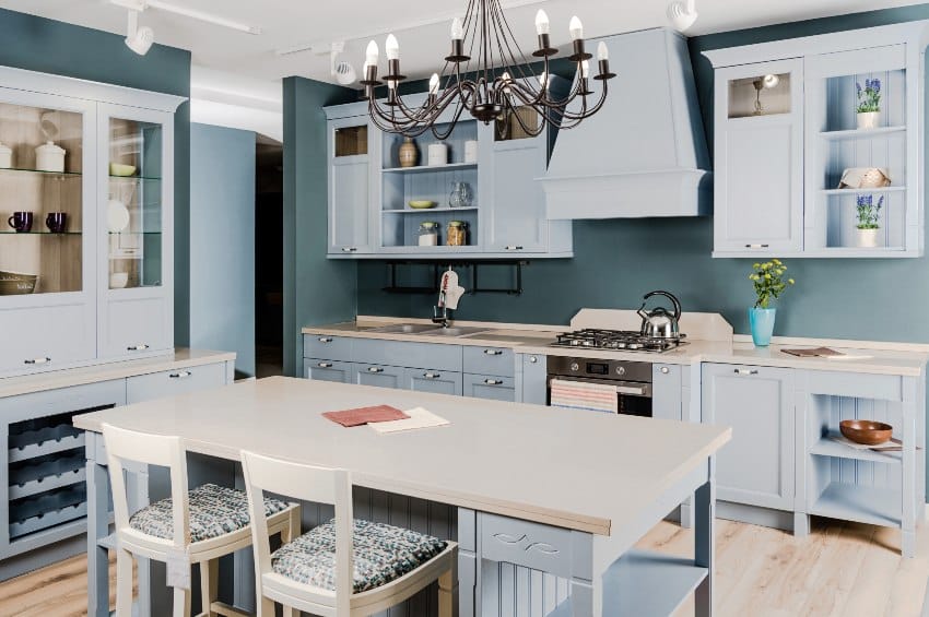 Simple light blue kitchen with wooden floors, island with chair and kitchen cabinets with legs
