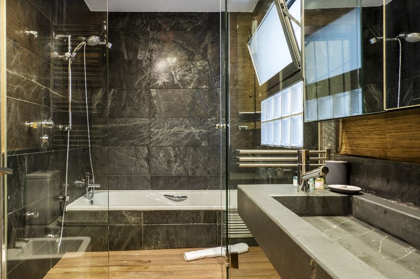 Bathroom with black wall tiles, wood plank flooring and cabinets with mirrored doors