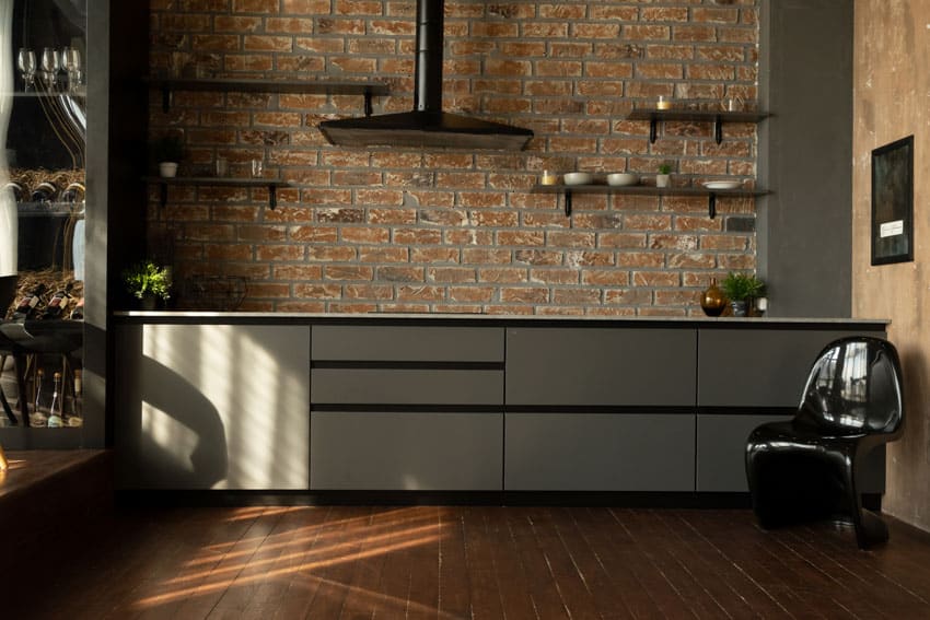Small industrial kitchen with brick backsplash, floating shelves, cabinets, range hood, and wood floors