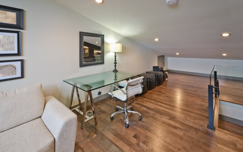 Spacious attic office with glass desk, couch, chair, lamp, recessed lights, and wood floors