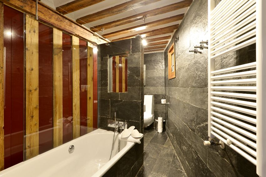 Bathroom with slate tiles on walls and floors, built in white bathtub and ceiling with wooden beams