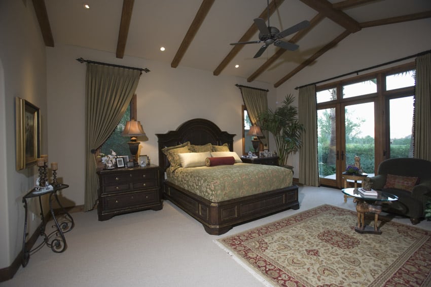 Spanish style bedroom with ceiling fan, nightstands, headboard, windows, curtains, lamps, and chair