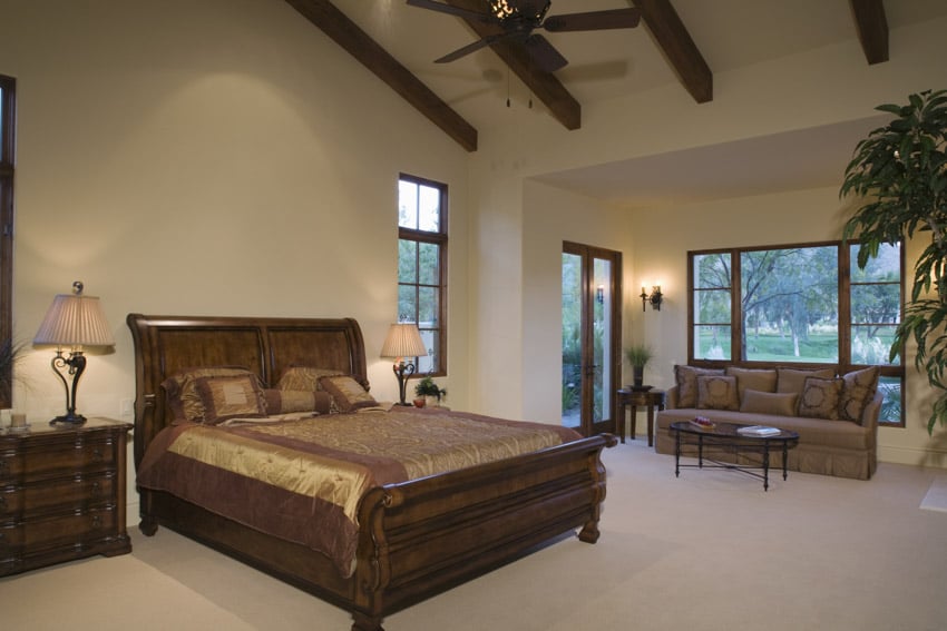 Spanish style bedroom with couch, coffee table, nightstand, lamp, ceiling fan, exposed ceiling beams, and windows